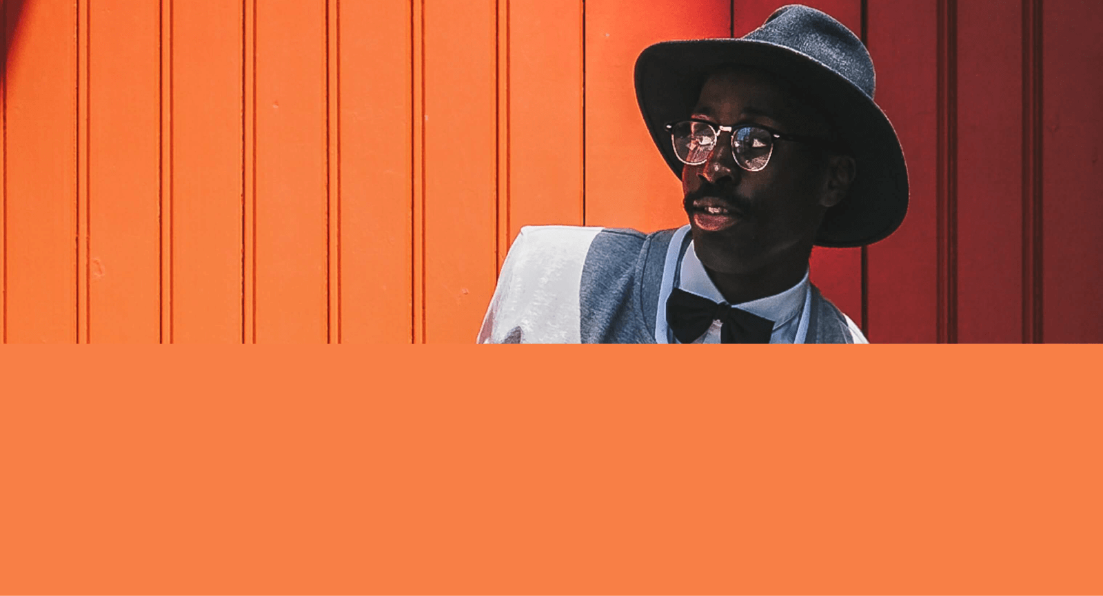 Foto de um modelo negro, vestido de roupa de paleta branca e fundo laranja