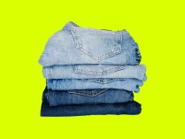 Imagem de calças jeans de cor azul fosco e calças jeans  de cor de azul escuro, as calças jeans de amabas as tonalidades estão dobradas numa pilha de clças jeans, com fundo verde neon